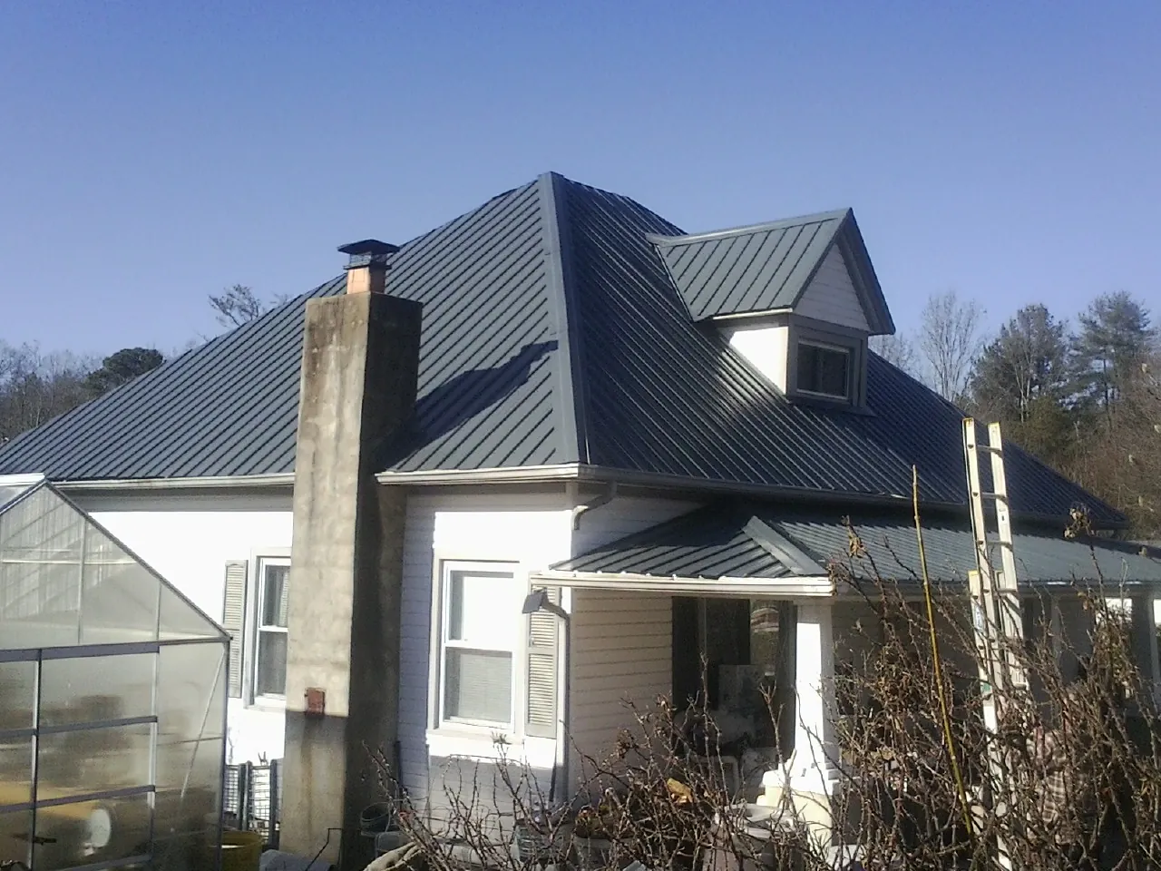 Dark blue standing seam metal roof on a white farmhouse with dormer — Slate & Tile Roof Repair by Roofing Brothers in Healdton
