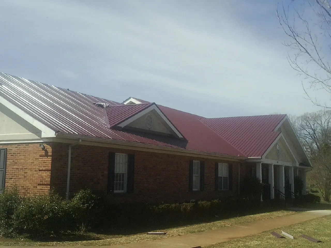 Red metal roof with gabled entries on a long brick building, from a Hail Damage Roof Repair job in Healdton