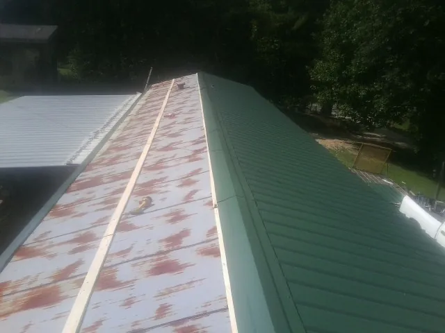 Old rusted panels beside newly installed green metal roofing — Wind Damage Roof Repair by Roofing Brothers in Healdton