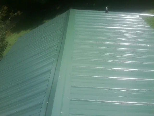 New green metal panels meeting at the ridge of a roof — Flat Roof Repair work by our crew in Healdton
