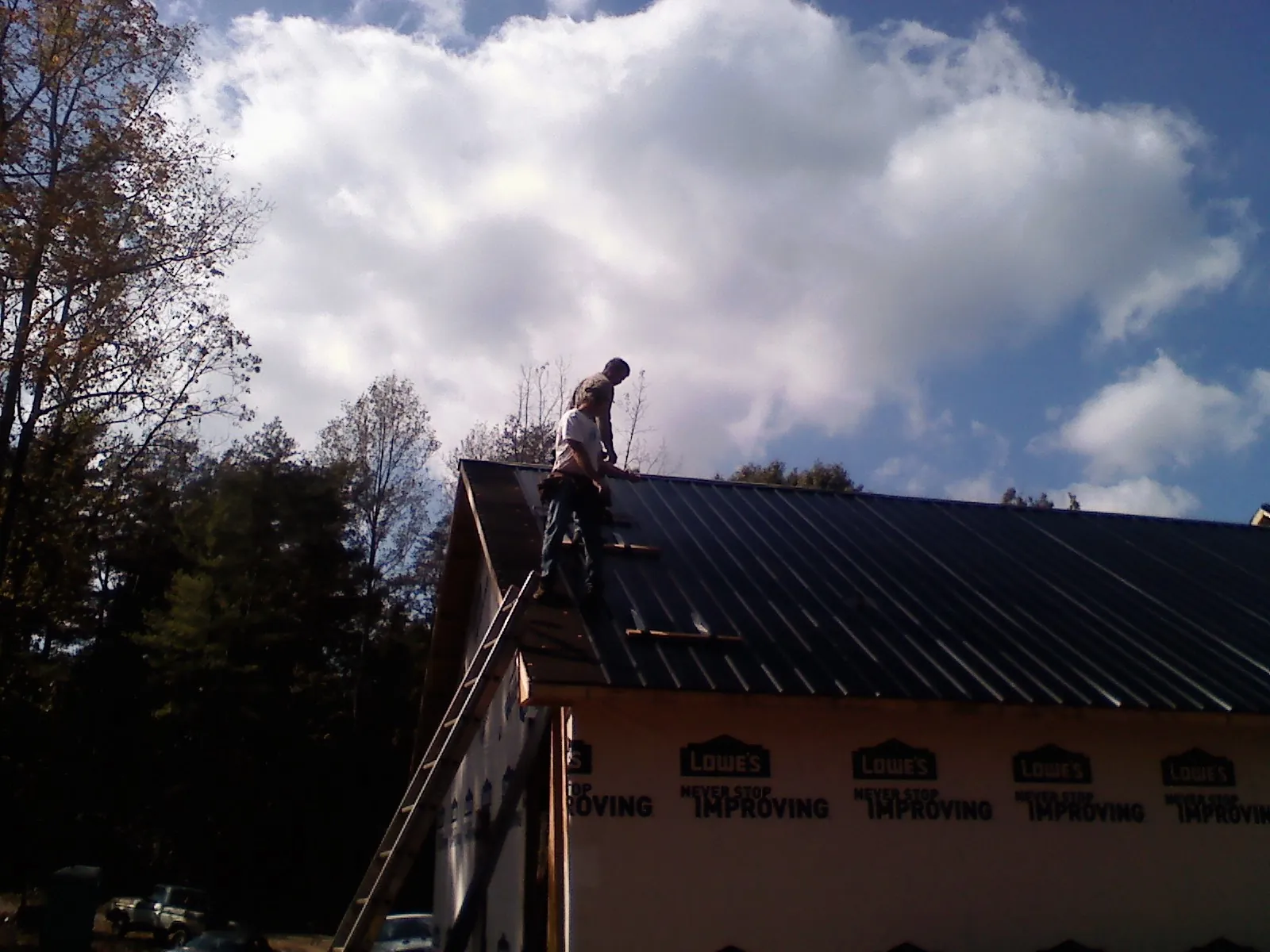 Roofer fastening dark metal panels high against a cloudy sky, from a Roof Inspection job in Healdton