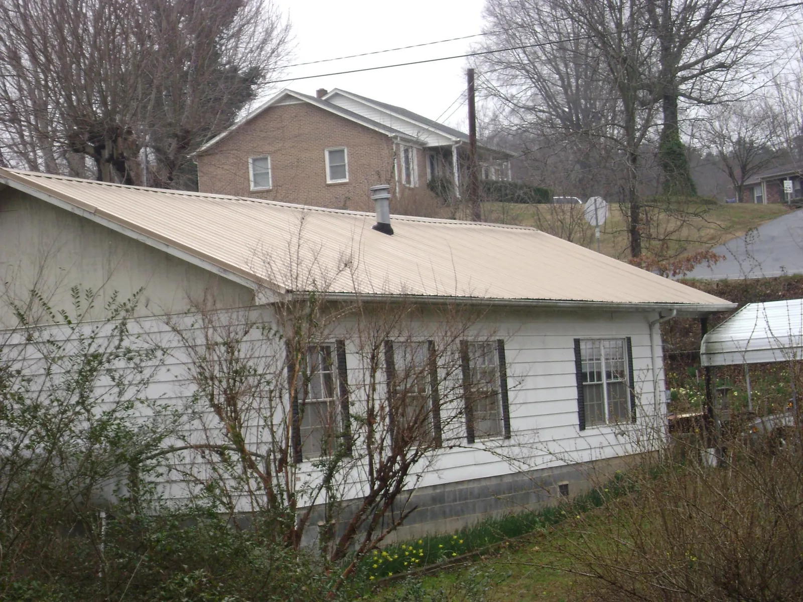 Tan metal roof on a white sided house set into a hillside — Commercial Roofing by Roofing Brothers in Healdton