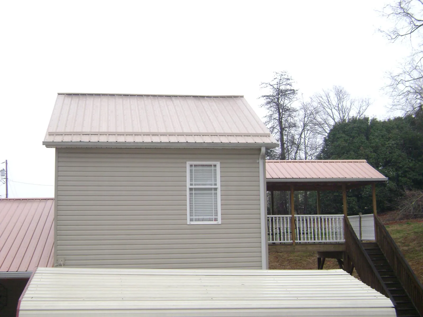 Tan metal roofs on a two story addition and attached porch, from a Roof Replacement job in Healdton